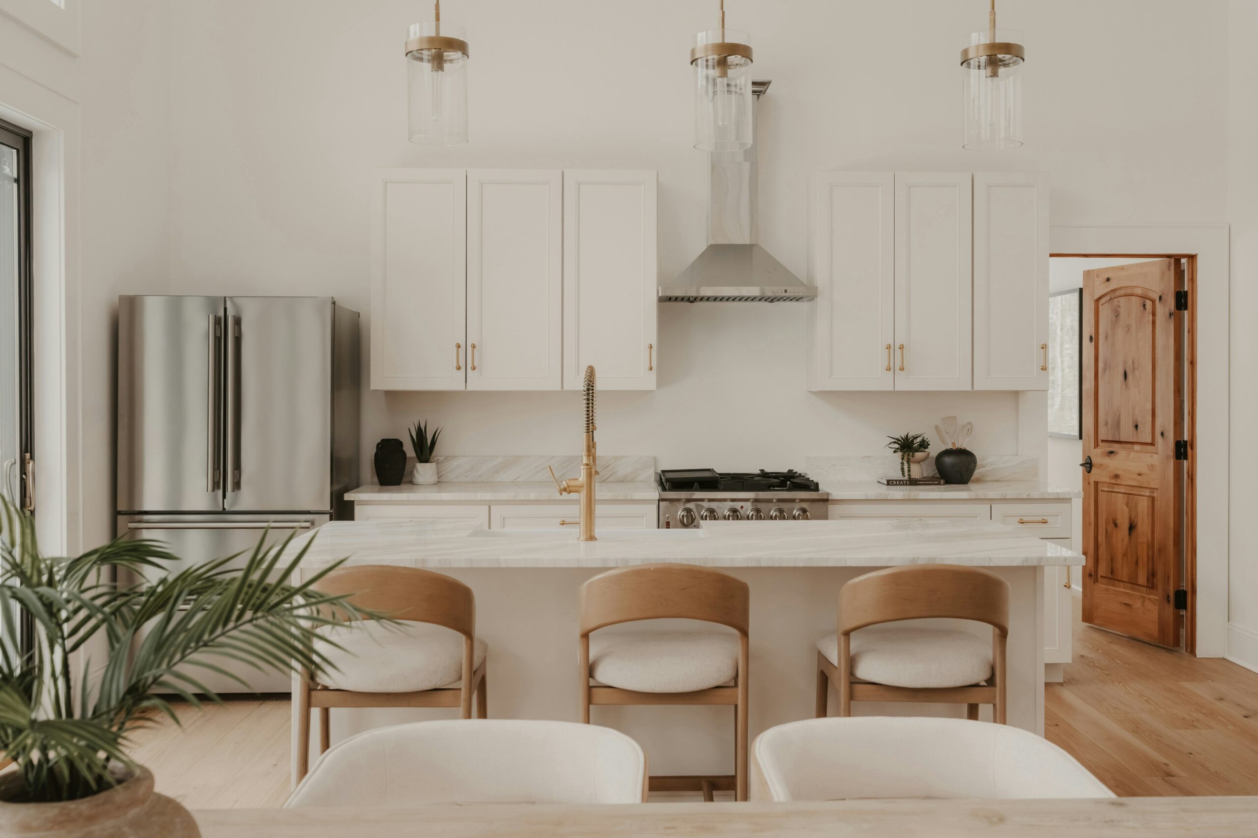 White kitchen with a marble island, three wood bar stools, and brass fixtures styled for a local furniture sale in Chicago.