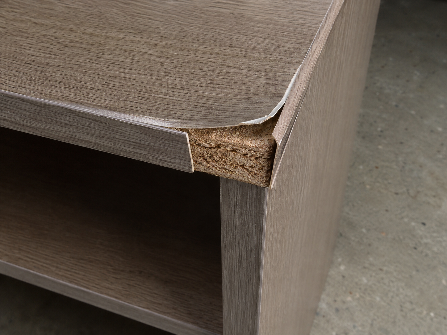 Particle board furniture edge with laminate peeling back, exposing the composite substrate beneath.